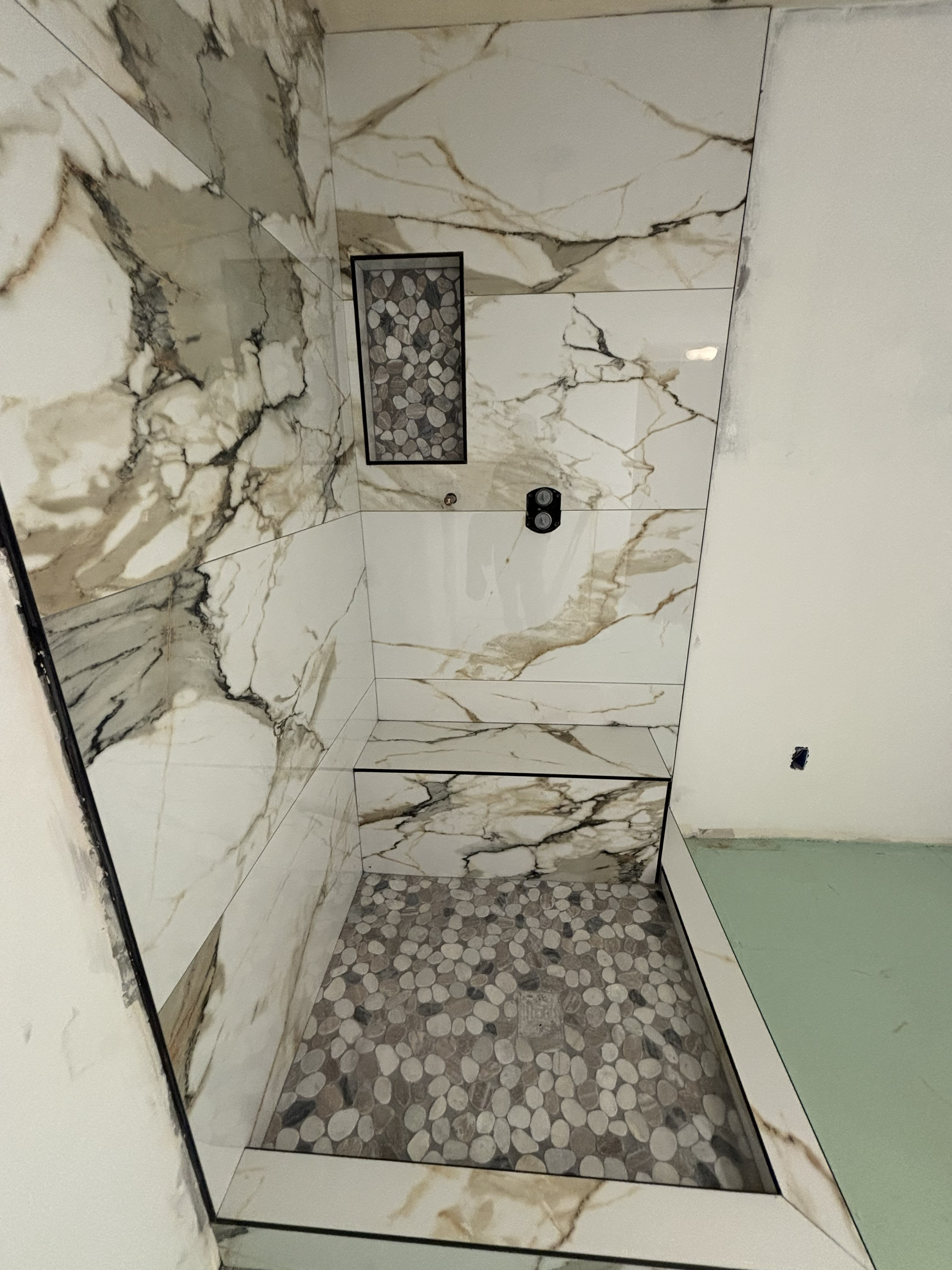Luxury marble shower remodel with pebble stone floor and matte black fixtures